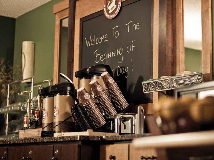 Una estación de café con un pizarrón que dice “¡Bienvenido al comienzo del día!” y diferentes equipos para preparar café.