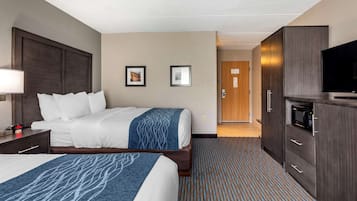 A hotel room with two beds, a desk with a lamp, a microwave, and a TV.