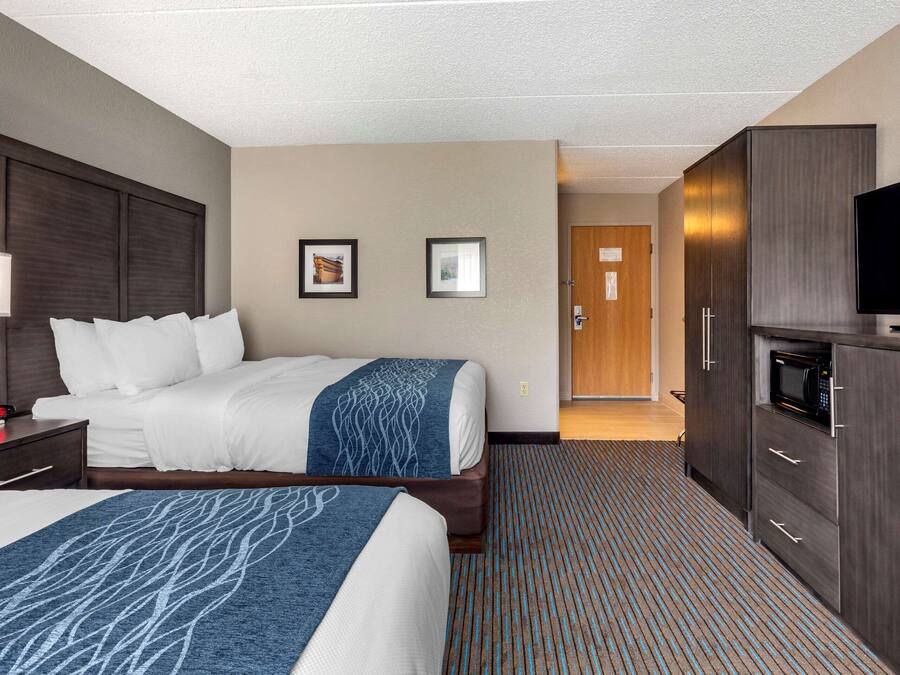 A hotel room with two beds, a desk with a lamp, a microwave, and a TV.