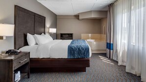 Habitación de hotel con una cama grande, una mesita de noche con lámpara, un escritorio pequeño con teléfono, televisión y un baño con bañera y ducha.
