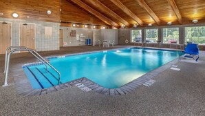 Una piscina interior con techo de madera, una silla de salvavidas y una zona junto a la piscina con mesa y sillas.