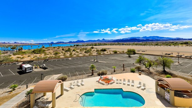 A pool area with lounge chairs, a hot tub, and a view of mountains and a parking lot. - Studio 6 Suites Lake Havasu City, AZ  (Lake Havasu City)