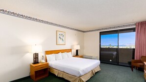 A hotel room with a large bed, two bedside tables with lamps, a small desk, a chair, and a large window with a view of the beach. - Studio 6 Suites Lake Havasu City, AZ  (Lake Havasu City)