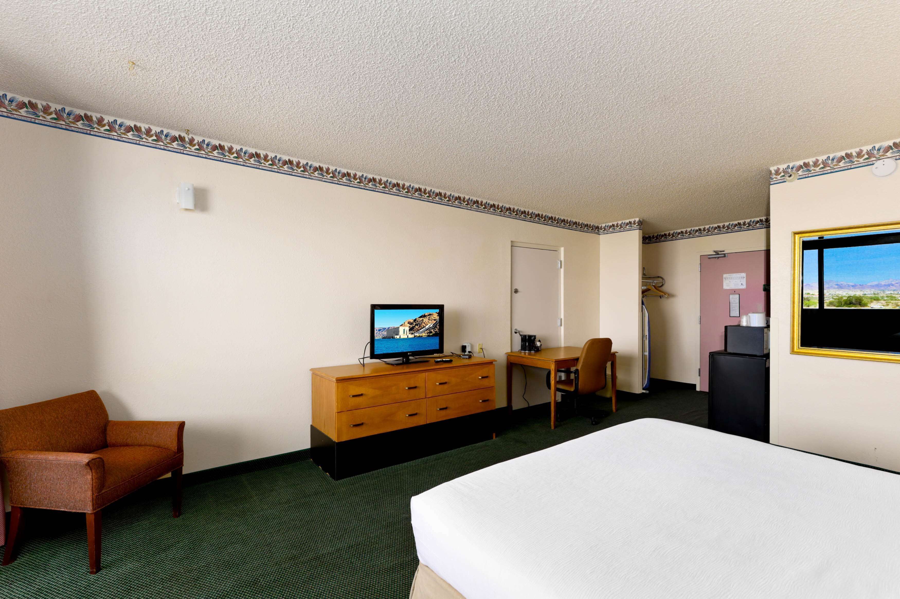 A hotel room with a bed, a wooden dresser, a television, a desk, and a chair.