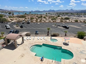 Zona de piscina con sillones de descanso y una piscina pequeña, rodeada por un estacionamiento y un paisaje desértico con montañas al fondo.