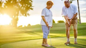 Two people on a golf course with a clear sky and sunlight.