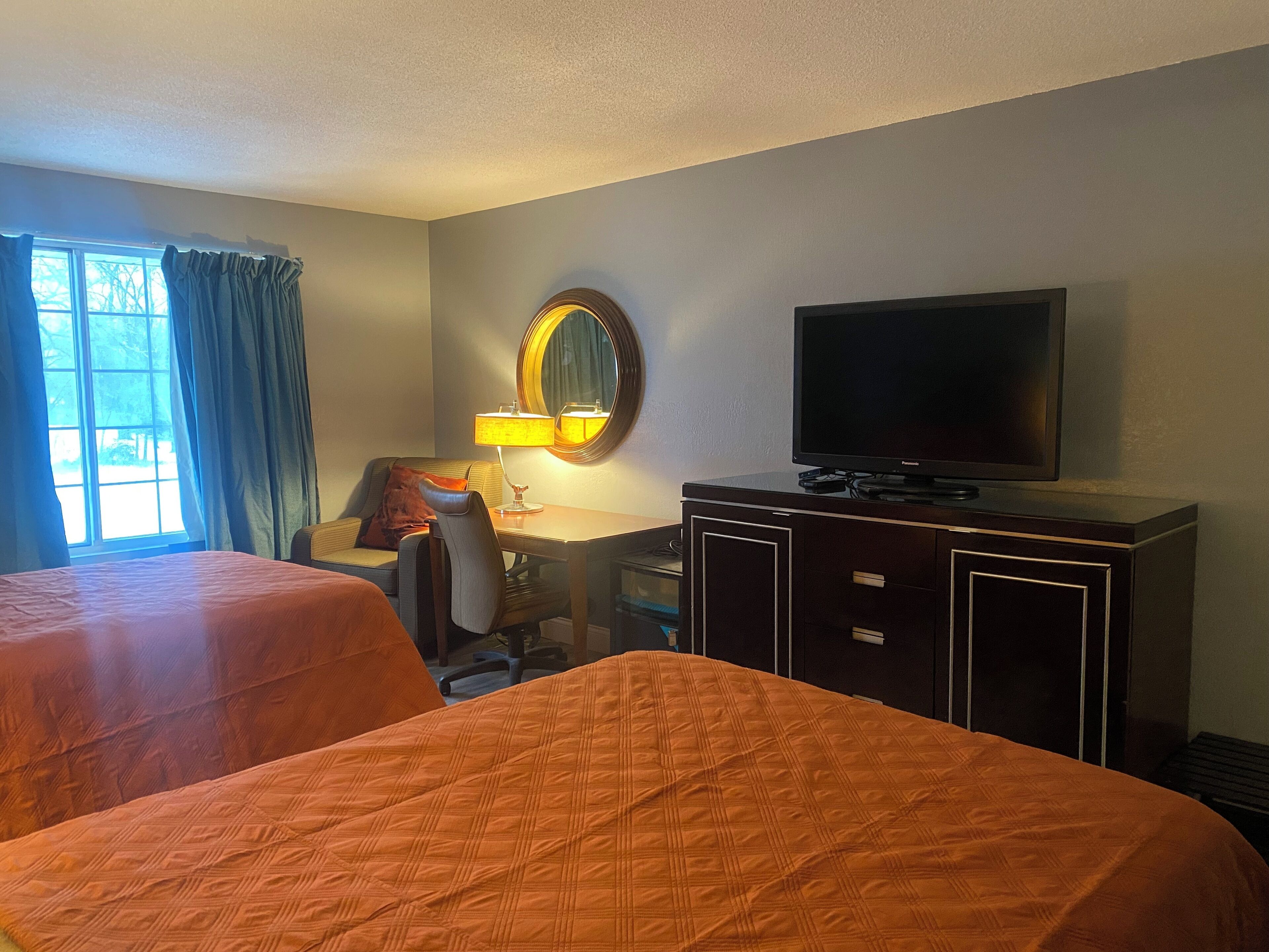 Een hotelkamer met twee bedden, een bureau met lamp, een televisie en een groot raam met gordijnen.