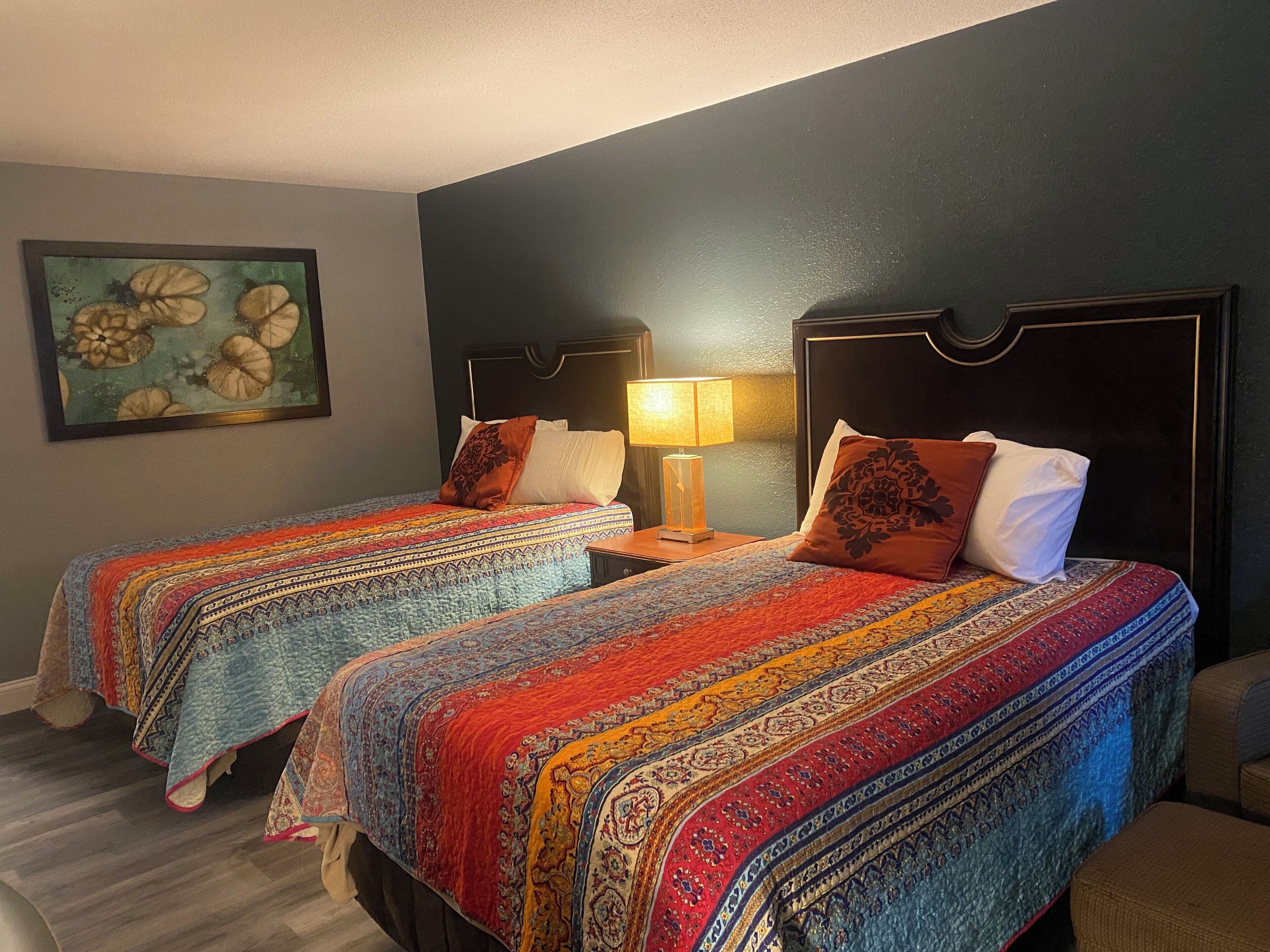 Une chambre d’hôtel avec deux lits, chacun recouvert d’une couvre-lit à motifs et agrémenté d’oreillers. Une table de chevet avec une lampe se trouve entre les deux lits.