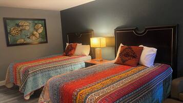 Une chambre d’hôtel avec deux lits, chacun recouvert d’une couvre-lit à motifs et agrémenté d’oreillers. Une table de chevet avec une lampe se trouve entre les deux lits.