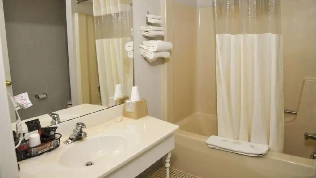 Un baño con lavamanos, espejo y cabina de ducha con cortina.