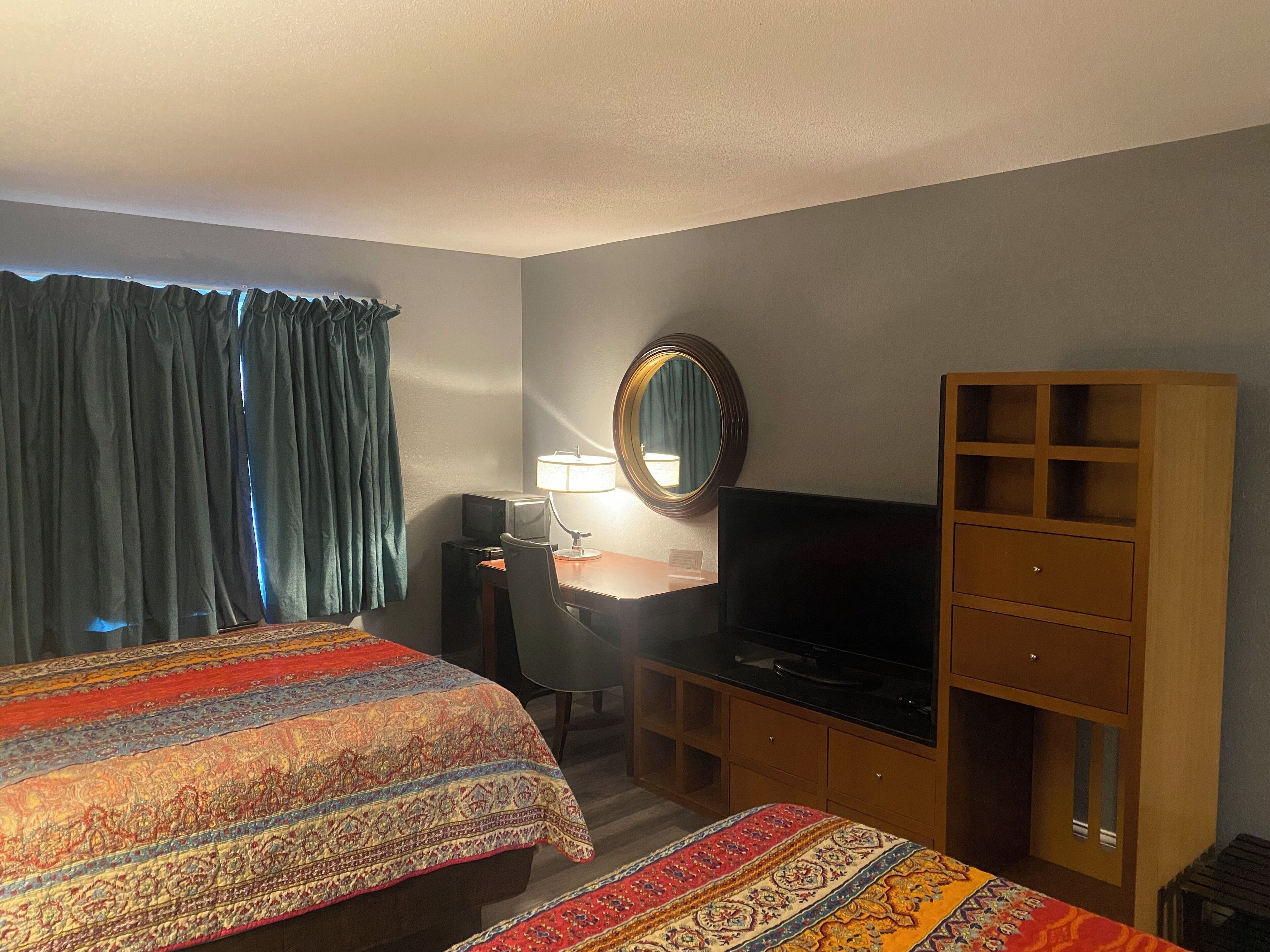 A hotel room with two beds, a desk with a computer, a television, a mirror, and a wooden cabinet.
