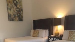 A hotel room with two beds, a patterned rug, a painting on the wall, and a nightstand with a lamp.