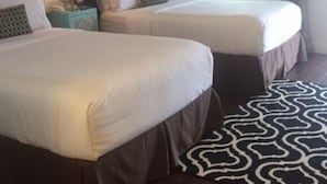 A hotel room with two beds, a patterned rug, and a nightstand with a lamp.