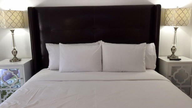 A neatly made bed with white linens and pillows, flanked by two bedside tables with lamps.