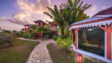 A pathway leading to a building with a red and white facade, surrounded by lush greenery and a clear sky.
