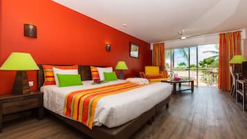 Quarto de hotel com uma cama grande, duas mesas de cabeceira, uma cadeira, varanda com vista e ventoinha no teto.