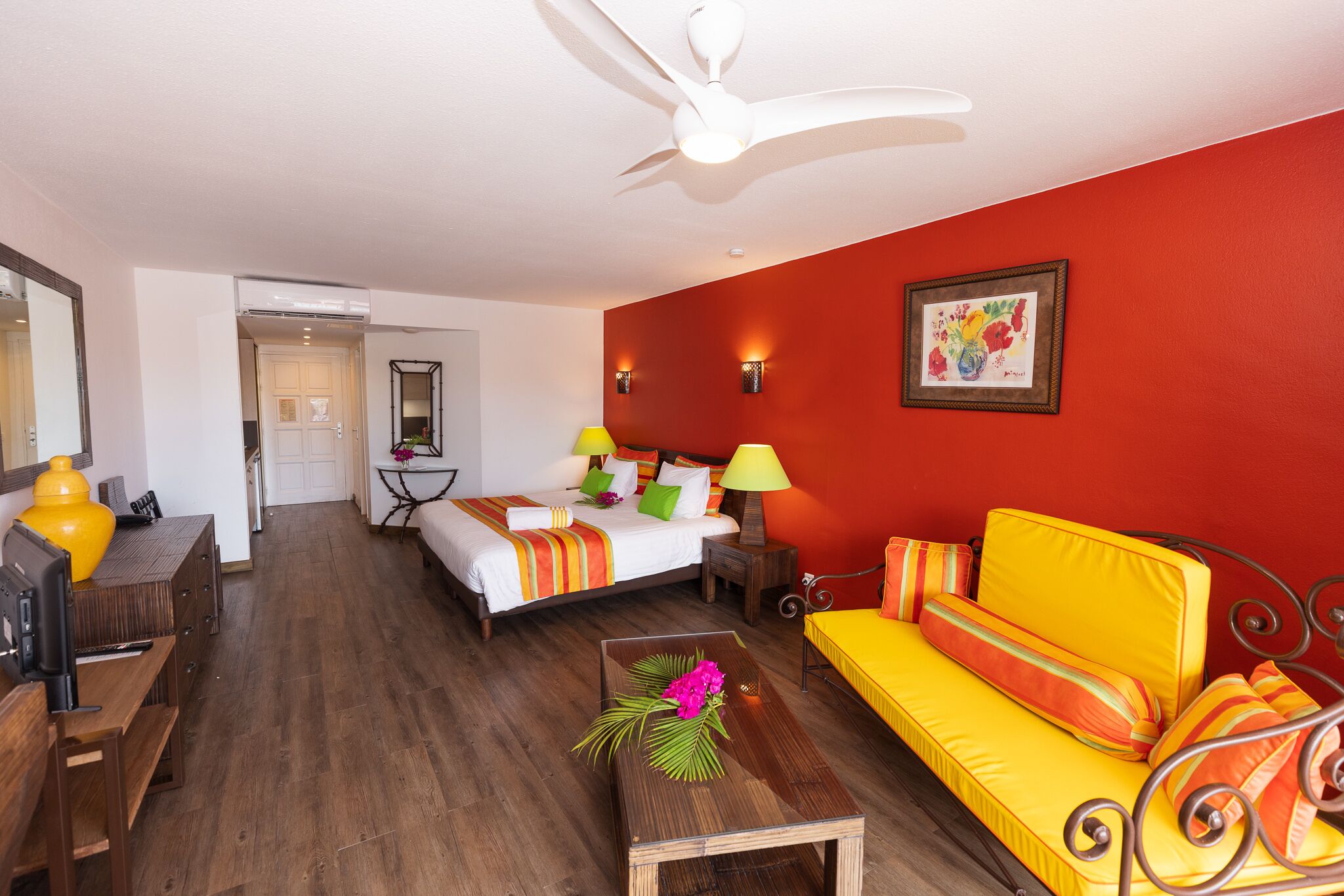 A hotel room with a bed, a sofa, a desk, and a ceiling fan.