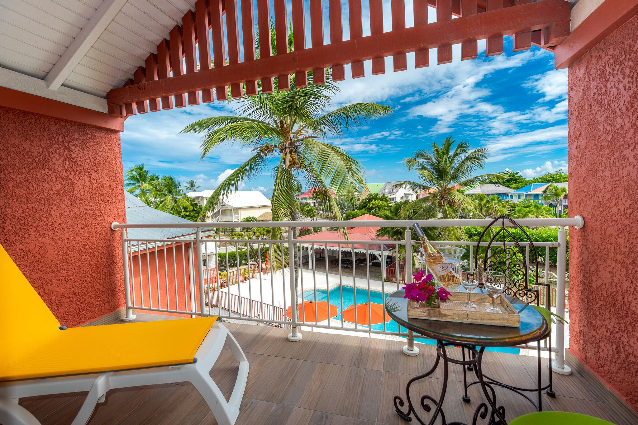A balcony with a pool, yellow lounge chair, and a table with drinks and flowers.