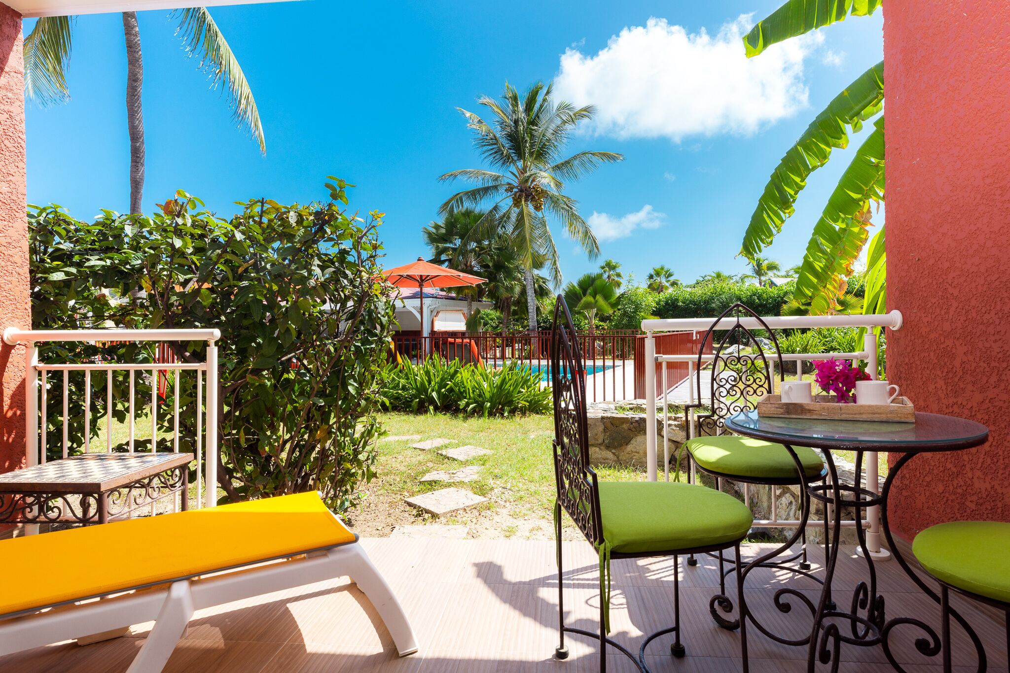 A patio with a white bench, a yellow lounge chair, and a table with green chairs.