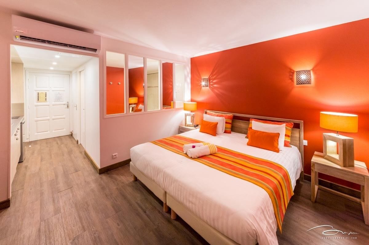 Habitación de hotel con una cama grande, un espejo, dos mesitas de noche con lámparas y suelo de madera.