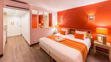 Habitación de hotel con una cama grande, un espejo, dos mesitas de noche con lámparas y suelo de madera.