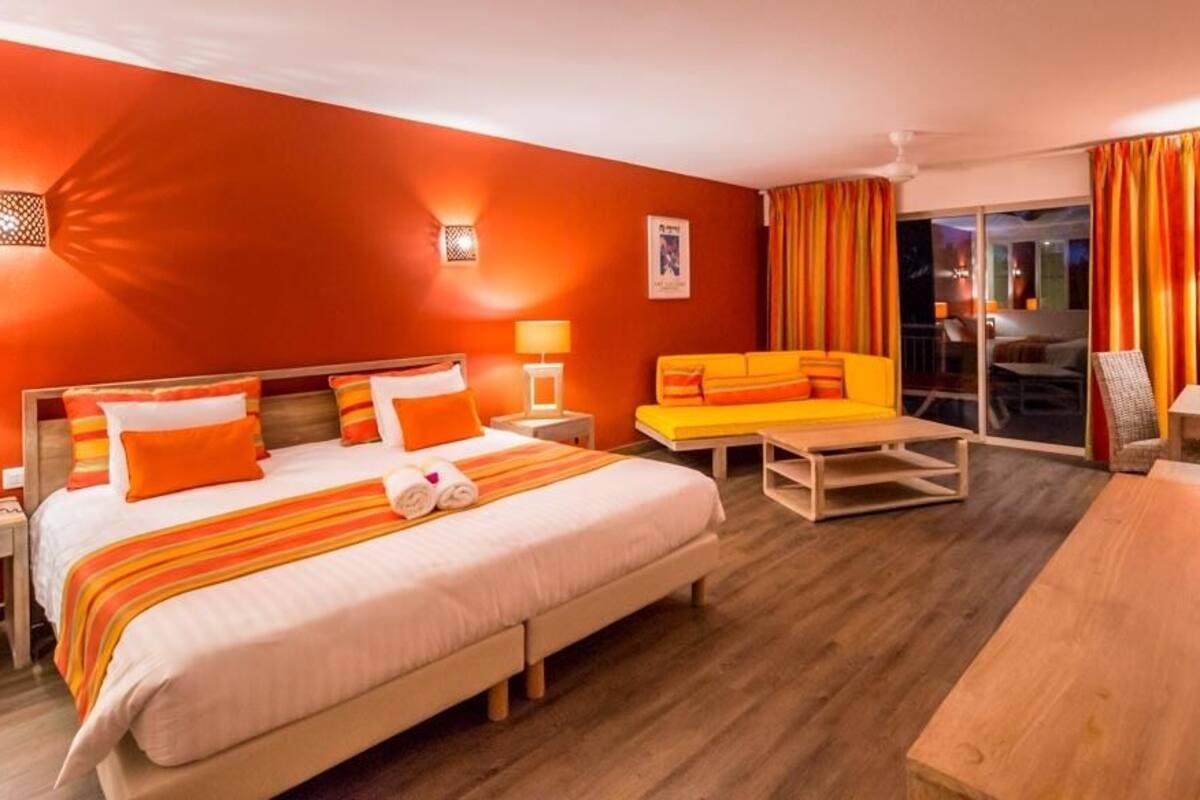 A hotel room with a large bed, a sofa, a desk, and a chair. There are two lamps on the desk and a TV on the wall.