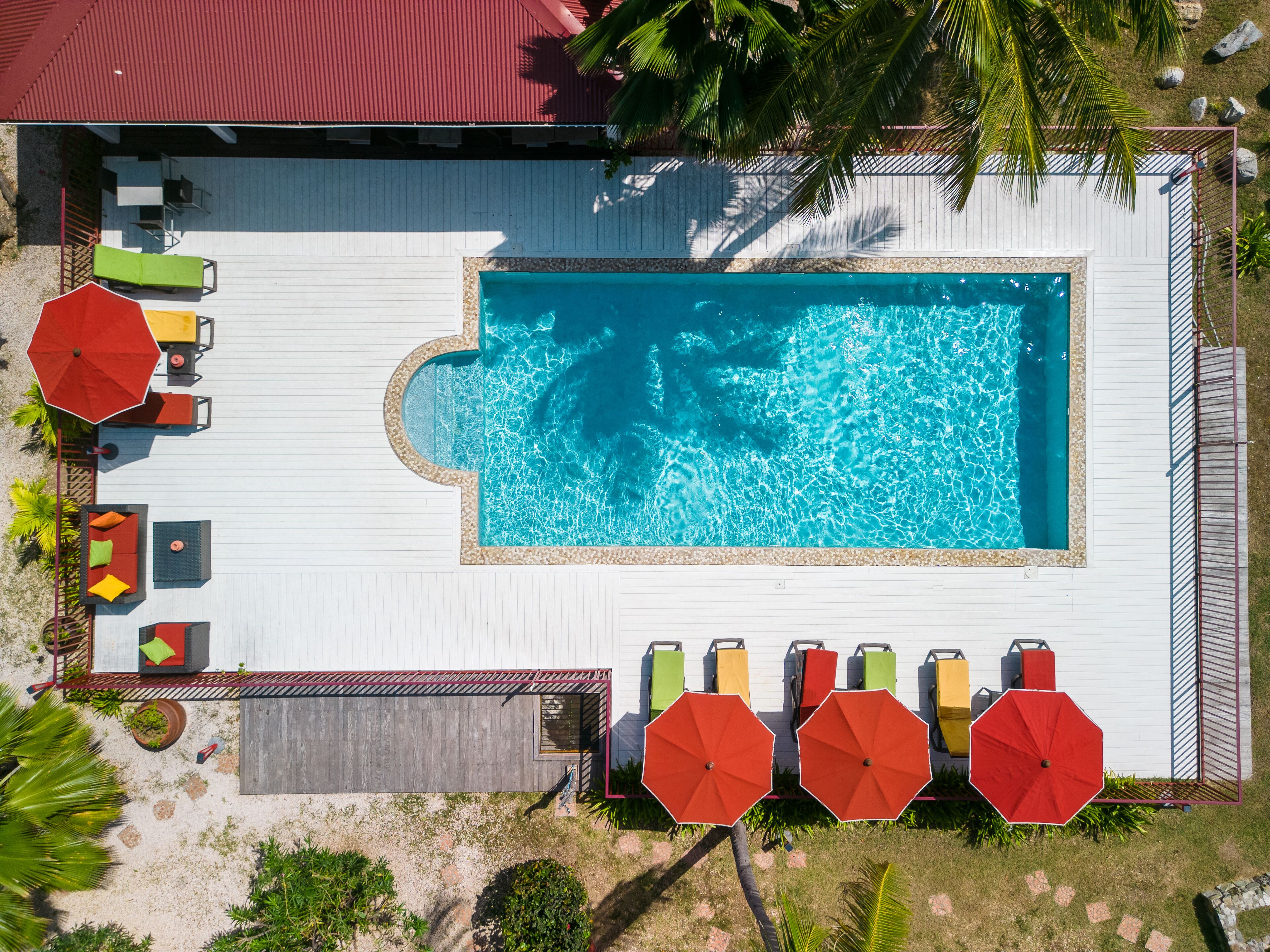 An aerial view of a swimming pool area with a deck, lounge chairs, umbrellas, and a small garden.