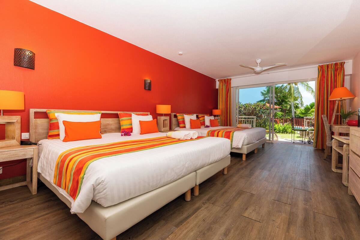 A hotel room with two beds, a balcony, and a view of the outdoors.