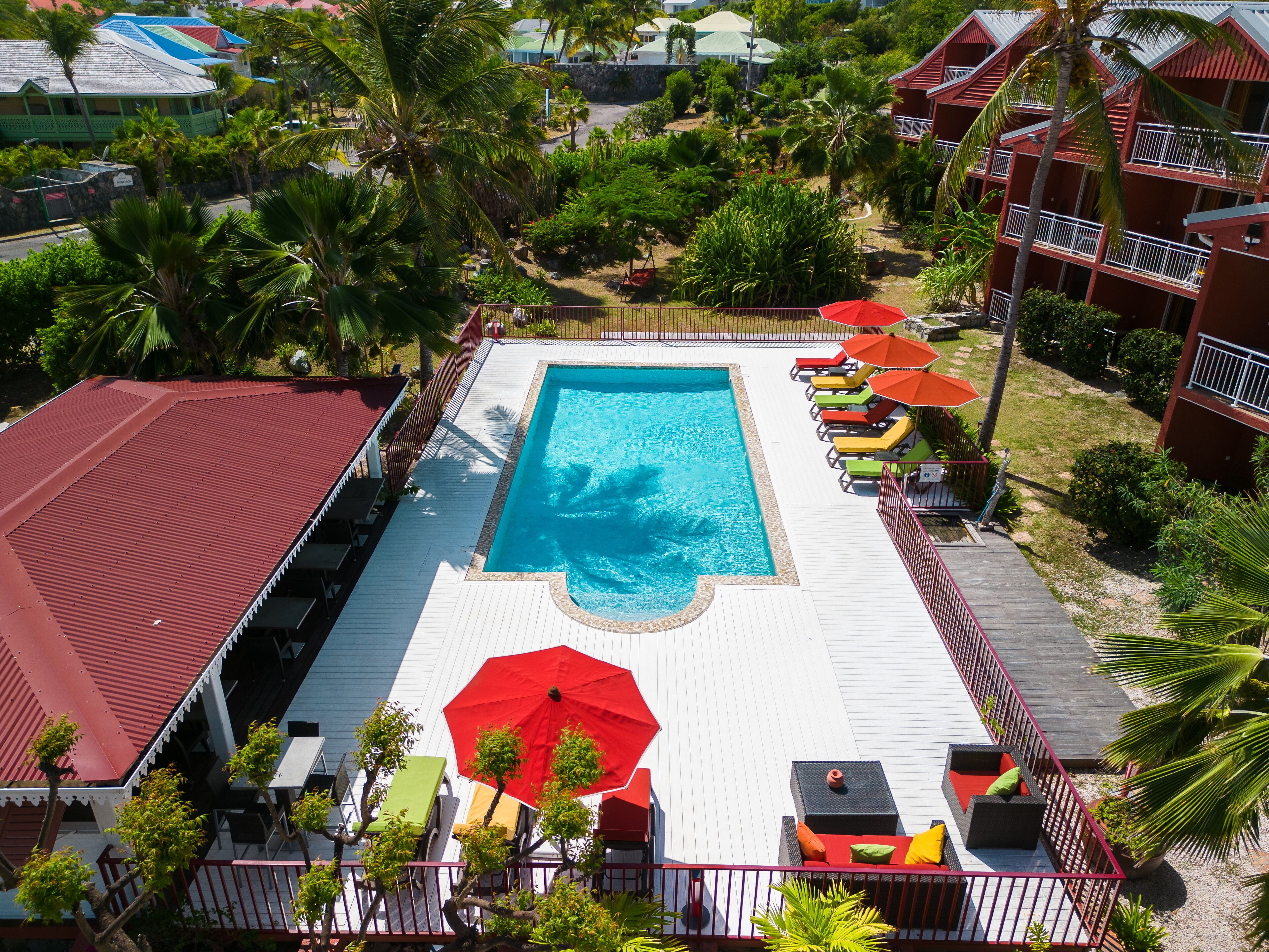 A swimming pool surrounded by lounge chairs and umbrellas, with a red-roofed building nearby.