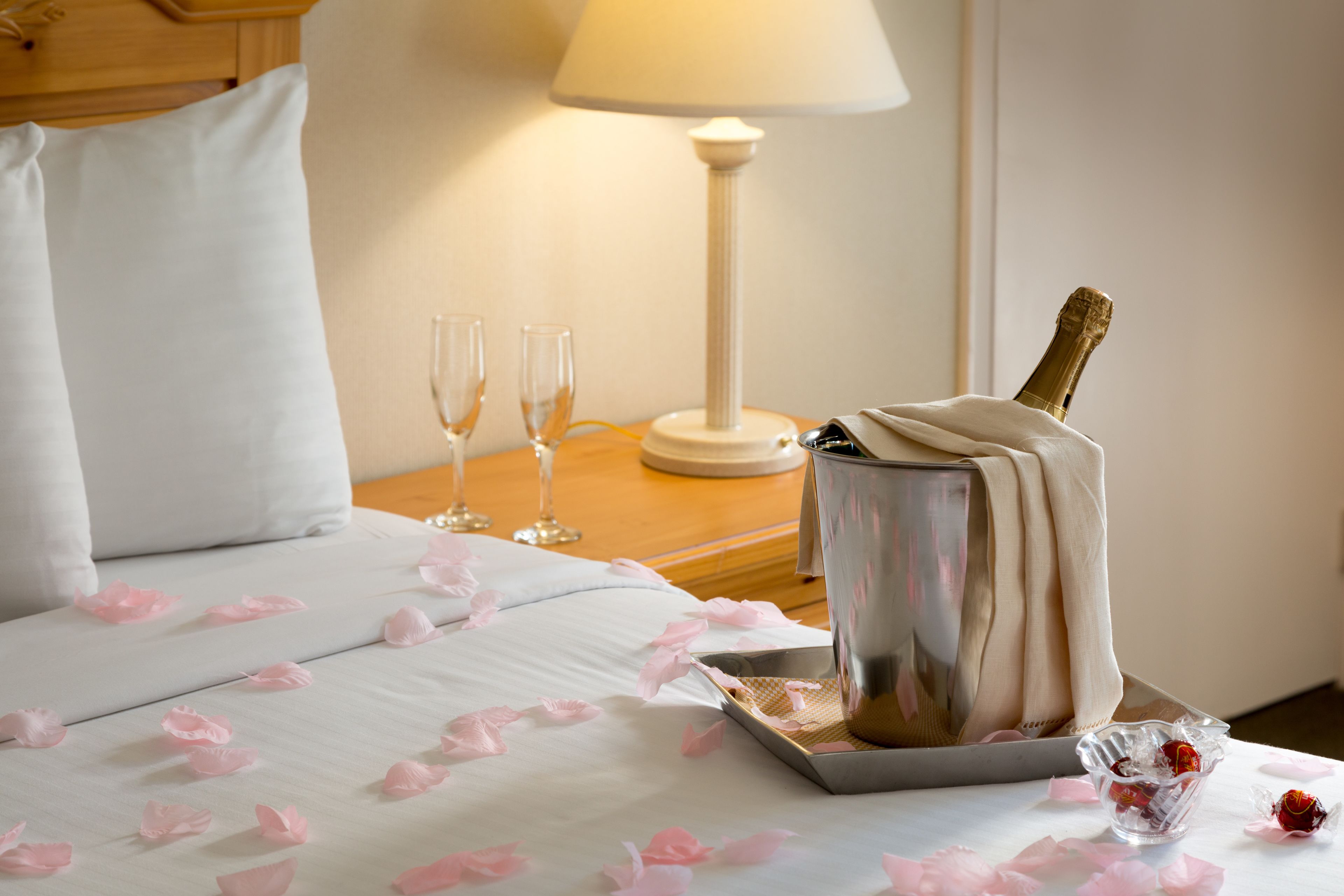 Une chambre d’hôtel avec un lit, une table de chevet avec une lampe, une bouteille de champagne et deux verres.