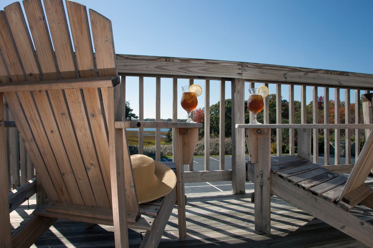 Een houten terras met een stoel, een tafel, twee glaasjes ijsthee en een strohoed.