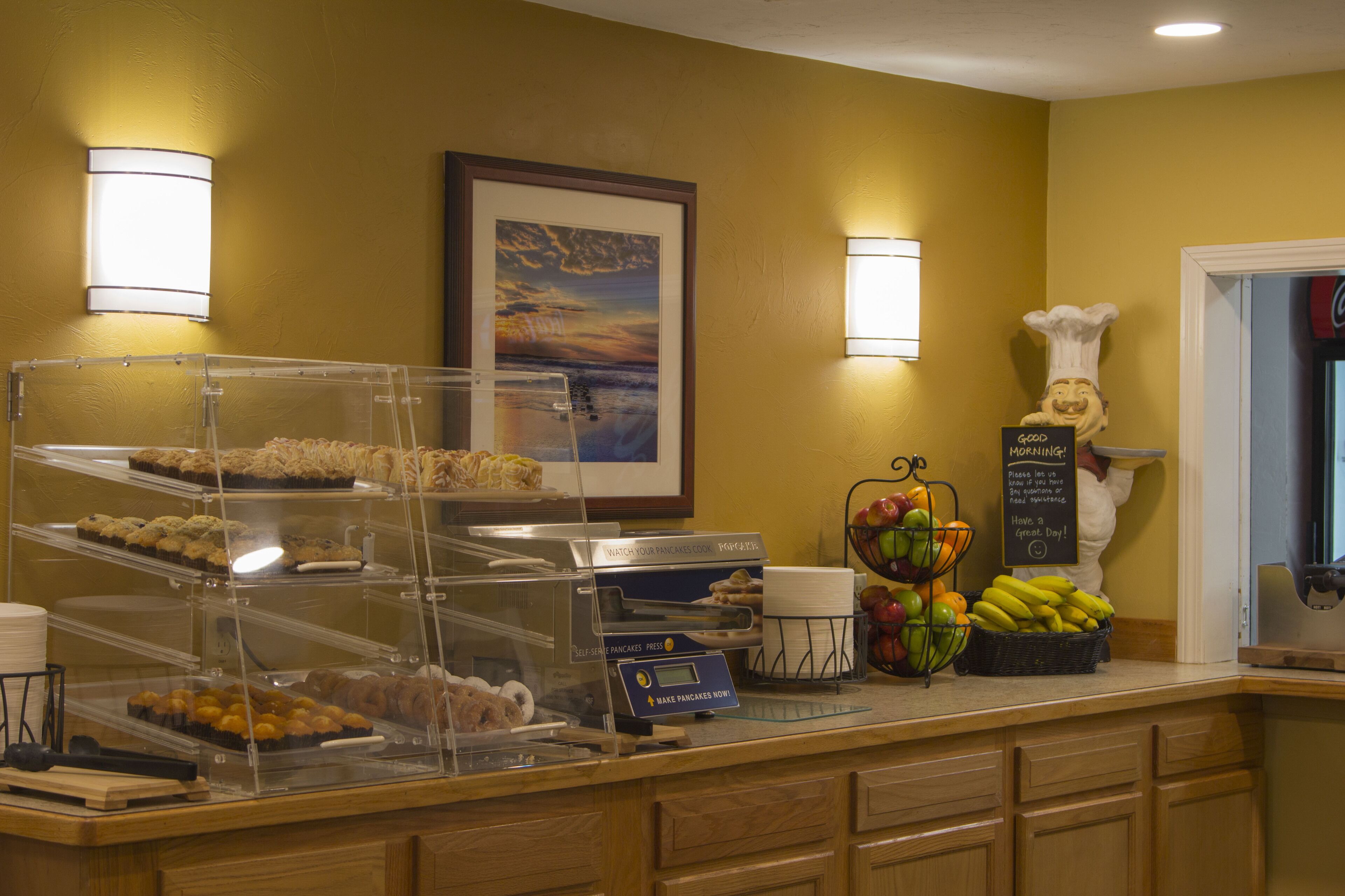 A breakfast buffet with various pastries, a self-serve pancake station, fresh fruit, and a chef mascot.