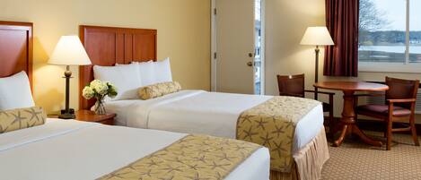 A hotel room with two beds, a desk, a chair, and a window with curtains.