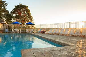 Una piscina con sillas de descanso blancas y sombrillas azules, rodeada por una cerca de metal.