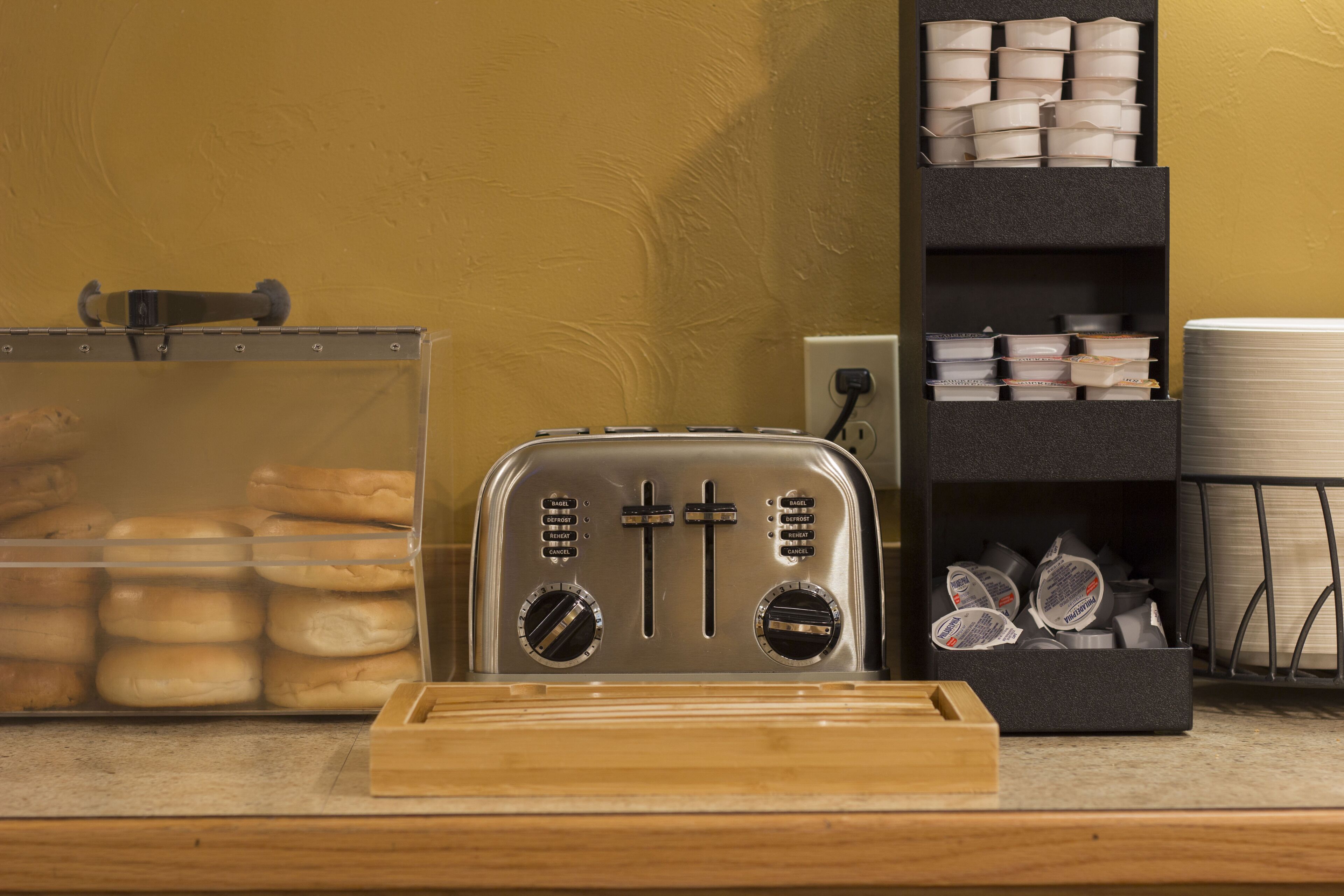 Un comptoir de cuisine avec un grille-pain, un présentoir à pain et une étagère contenant des récipients.