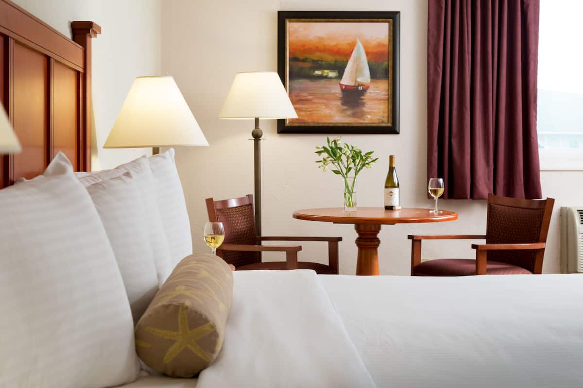 Hotelkamer met een bed, twee lampen, een tafel met een fles en een glas, en een schilderij aan de muur.