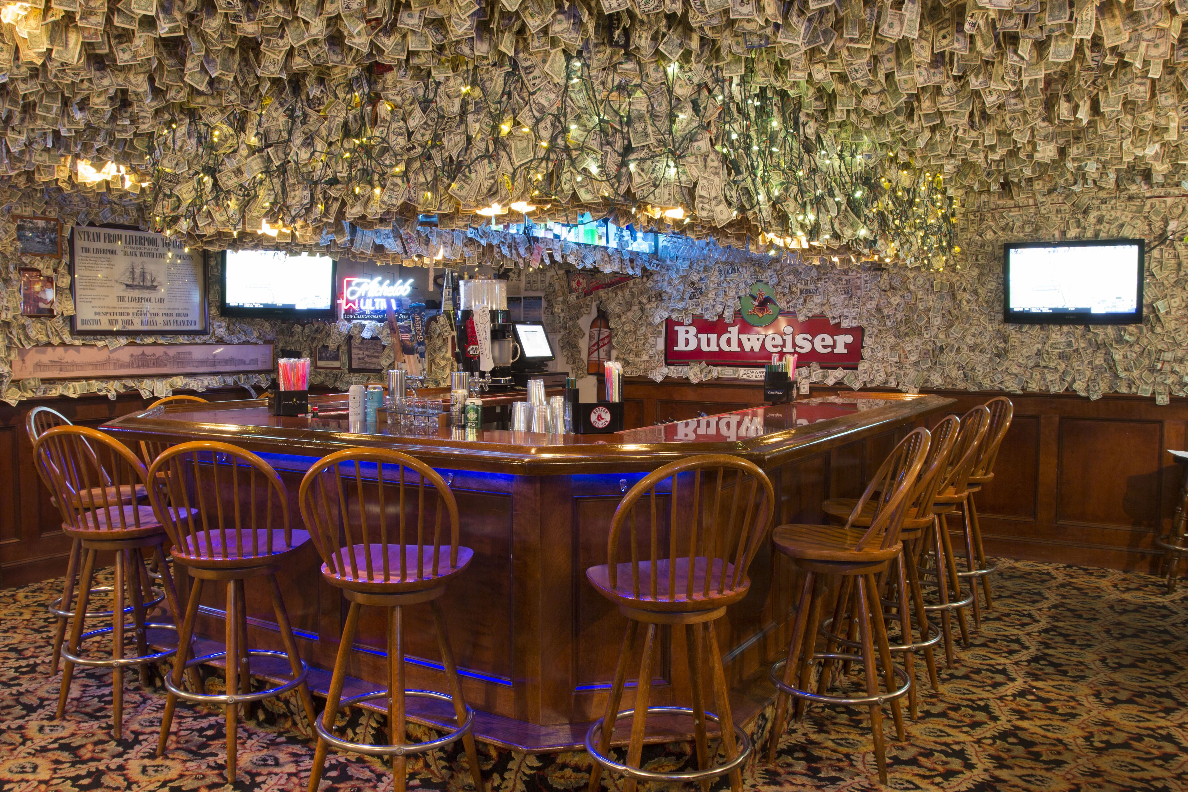 Un espace bar avec un comptoir en bois, plusieurs tabourets de bar et une enseigne Budweiser.