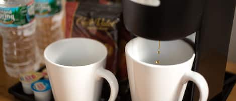 A coffee maker, two white mugs, and two water bottles on a tray.