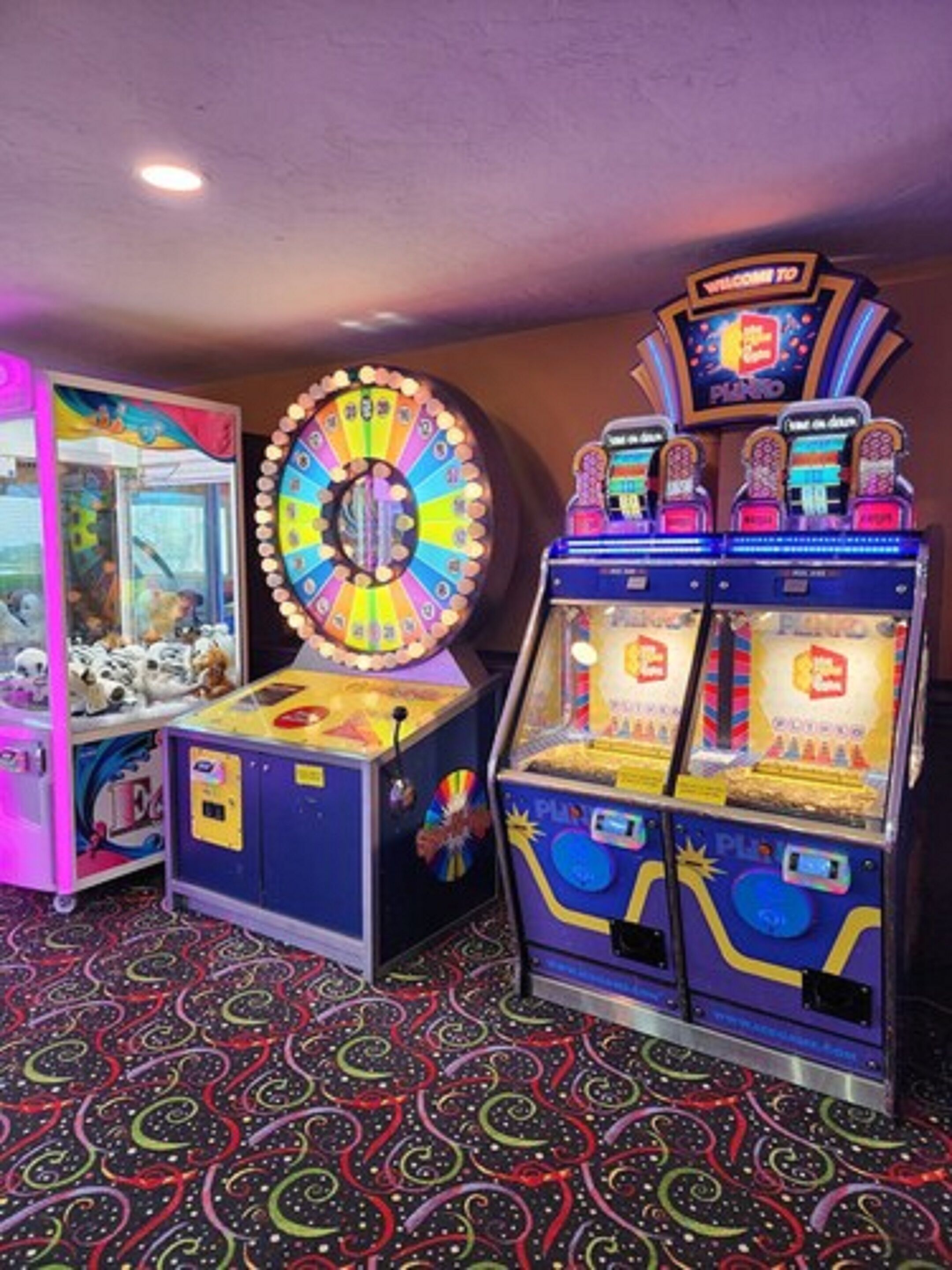 A room with arcade games, including a spinning wheel game and claw machines.