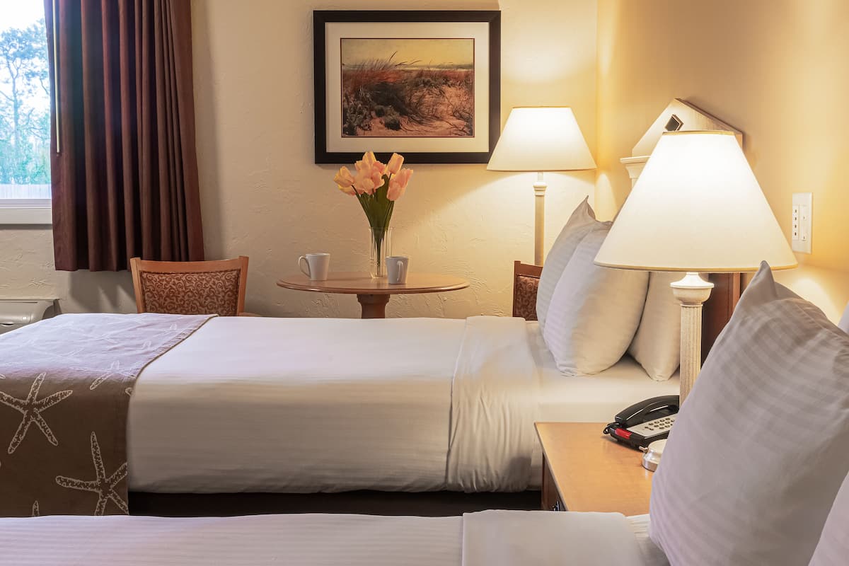 Hotelkamer met een bed, nachtkastje met lamp, bloemenvaas en een lijst met foto aan de muur.