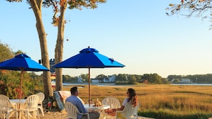 Een tafel aan het strand met twee stoelen, een blauwe parasol en een witte tafelkleed.