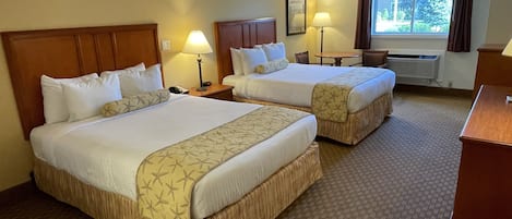A hotel room with two beds, a desk, a chair, a lamp, and a window with curtains.