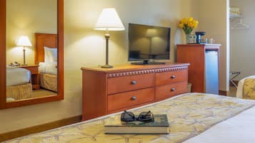A hotel room with a bed, a TV, a lamp, a dresser, and a mirror.