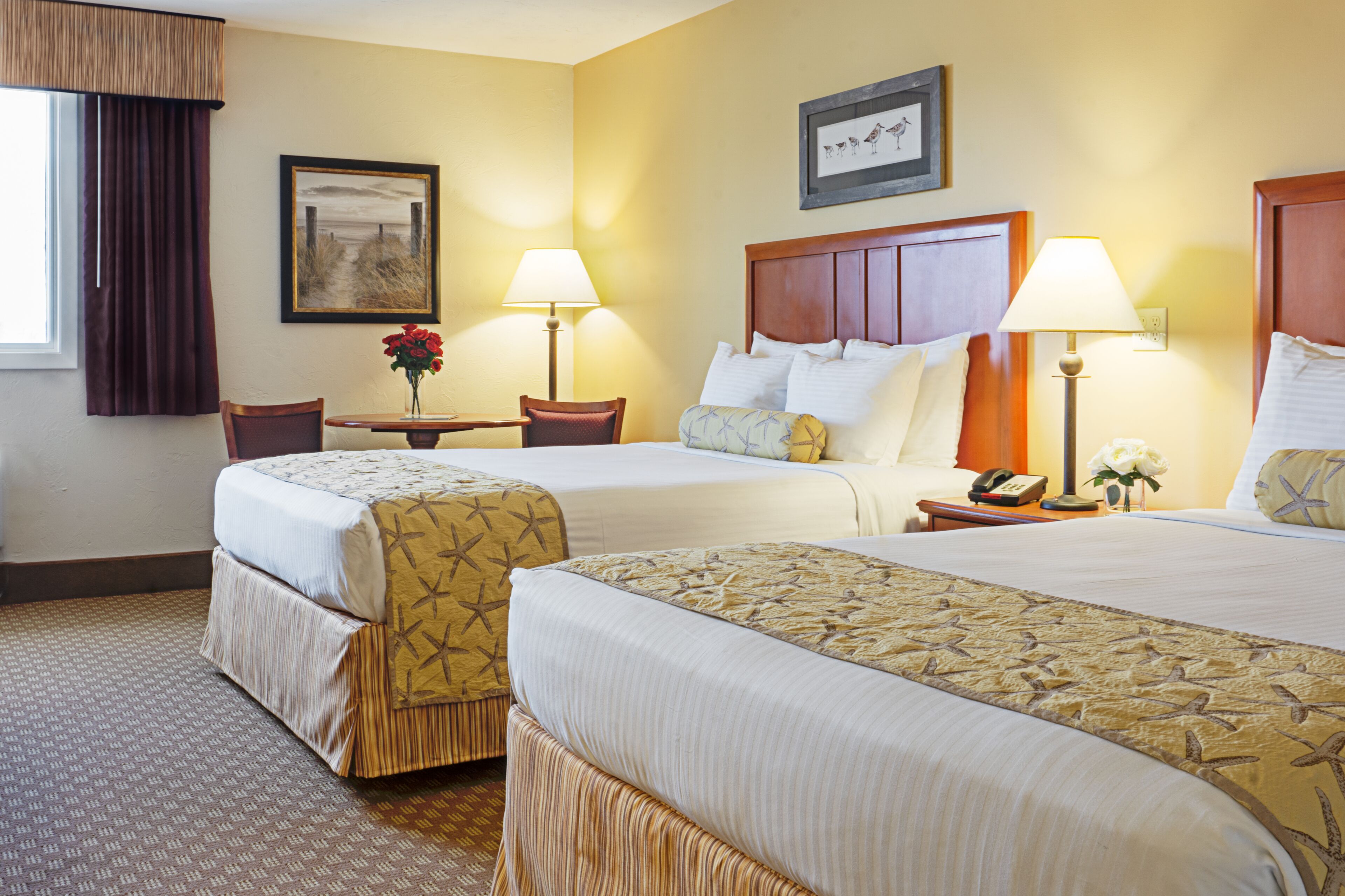 A hotel room with two beds, a desk with a lamp, a chair, and a framed picture on the wall.