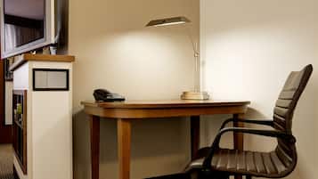 Una habitación de esquina con un escritorio de madera, una silla, una lámpara de escritorio y un teléfono.