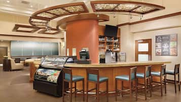 A bar area with a curved counter, bar stools, a coffee machine, and a refrigerated display case.