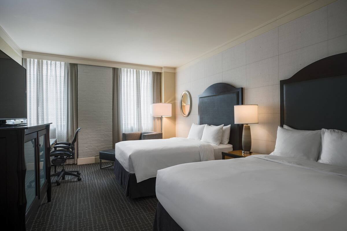 A hotel room with two beds, a desk, and a chair.