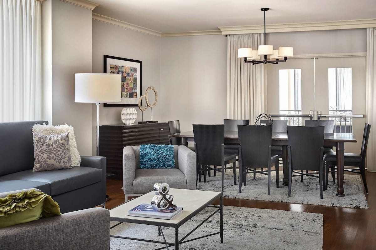 A modern living room with a grey sofa, a coffee table, and a dining area with a table and chairs.