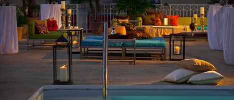 A rooftop pool area with lounge chairs, tables, and candles.