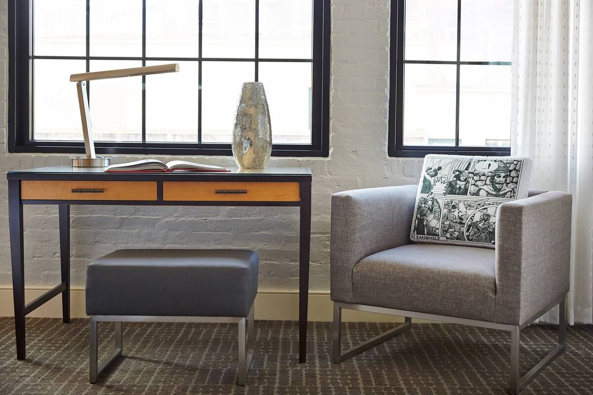 A room with a desk, a chair, a bench, a lamp, and a decorative vase.